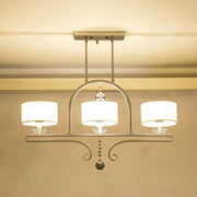 Modern brushed nickel island pendant light with three white fabric shades and crystal accents for dining room use