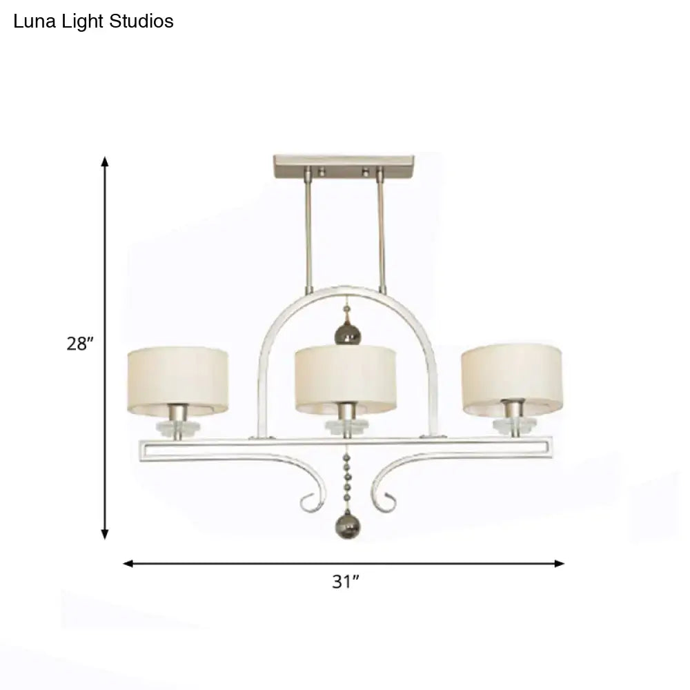 Modern brushed nickel island pendant light featuring a silver-toned wrought iron frame with three cream fabric shades and crystal accents