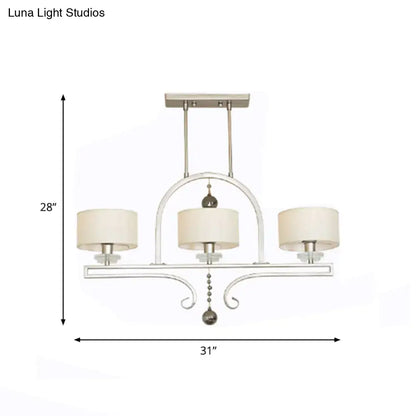 Modern brushed nickel island pendant light featuring a silver-toned wrought iron frame with three cream fabric shades and crystal accents