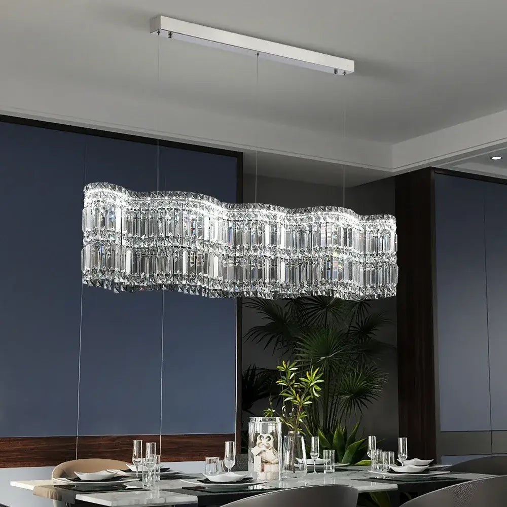 A modern brushed stainless crystal pendant light with clear glass prisms and wavy design for dining rooms