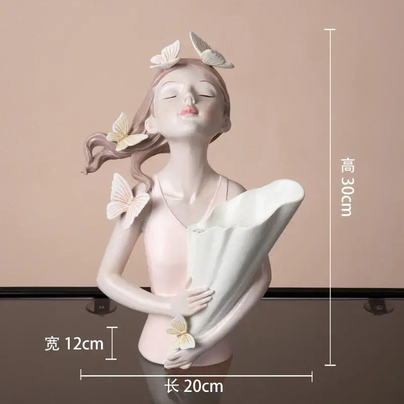 A delicate porcelain decorbites butterfly girl resin sculpture holding a white fan with pastel pink and cream tones