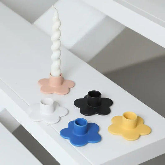 A set of five pastel and bold cartoon flower candle holders in matte plastic with one holding a white taper candle
