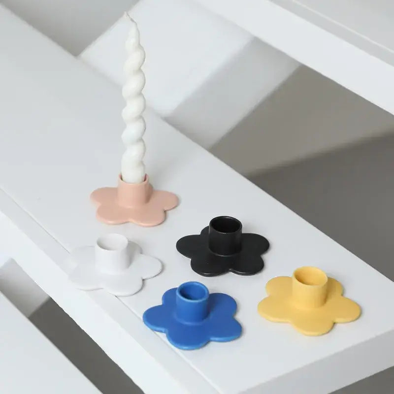 A set of five pastel and bold cartoon flower candle holders in matte plastic with one holding a white taper candle