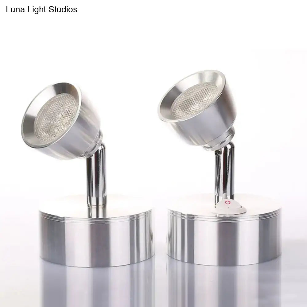 Two chrome adjustable spotlight wall sconces with metal shades and a small red power button emitting warm white light
