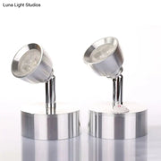Two chrome adjustable spotlight wall sconces with metal shades and a small red power button emitting warm white light