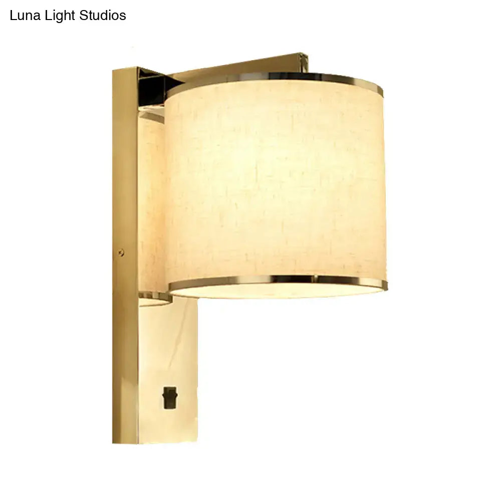 Gold-finished living room wall sconce with cylindrical off-white fabric shade and metallic rims in modern chrome style