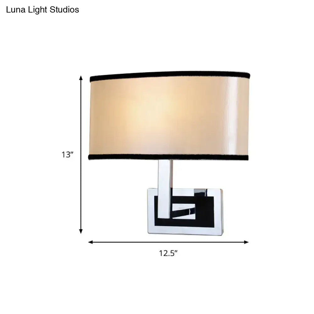 Modern chrome and beige oval wall sconce with cylindrical lampshade and black trim for bedroom lighting