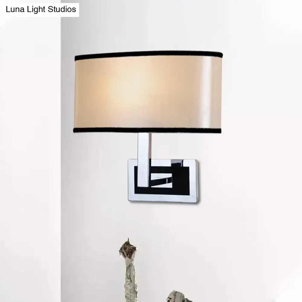 Modern chrome and beige oval wall sconce with a satin fabric shade and rectangular base for bedroom lighting