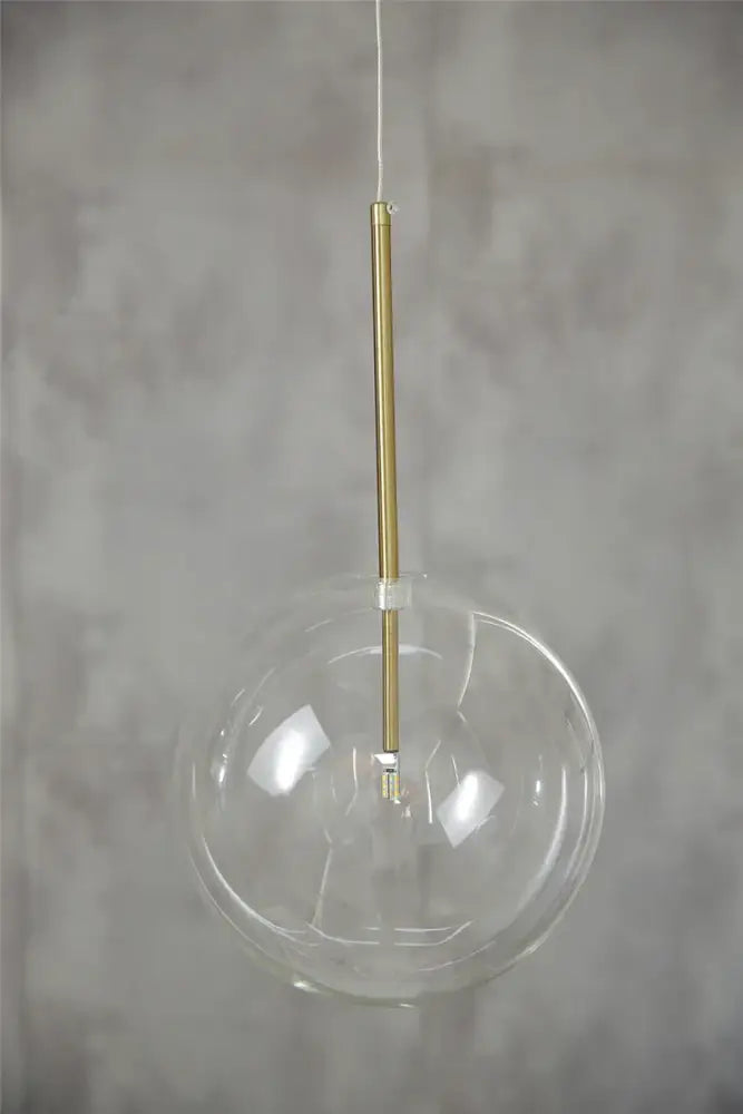 Modern chrome and brass pendant light with clear glass globe and slender brass rod for kitchen lighting