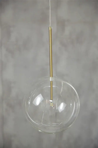 Modern chrome and brass pendant light with clear glass globe and slender brass rod for kitchen lighting