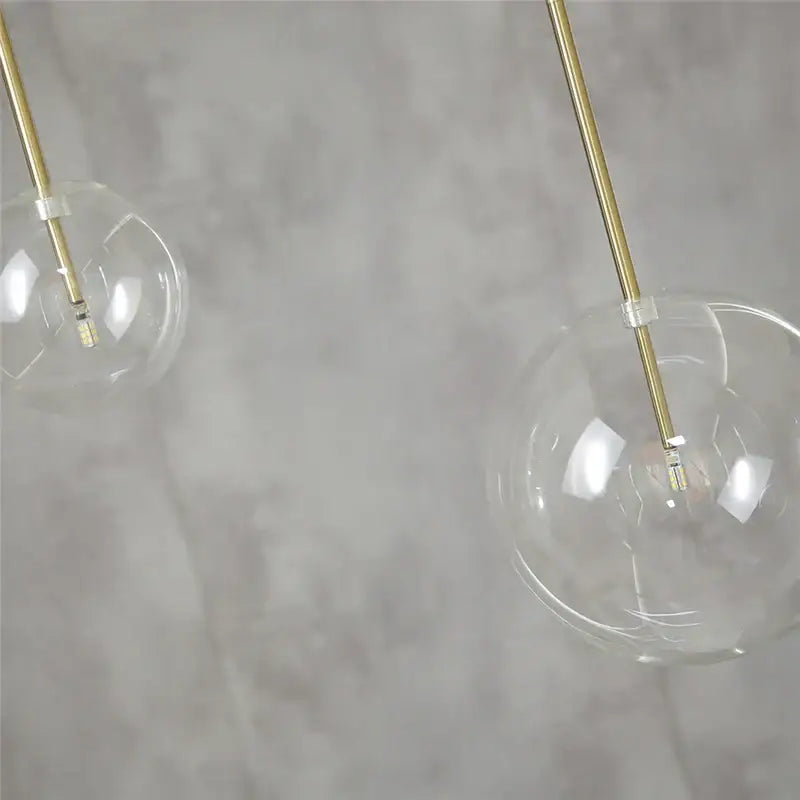 Modern chrome and brass pendant light with clear glass globe and slender brass rods for kitchen lighting