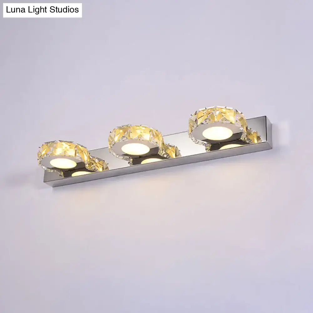 Modern chrome and gold crystal vanity sconce with three crystal-encrusted light fixtures emitting warm glow