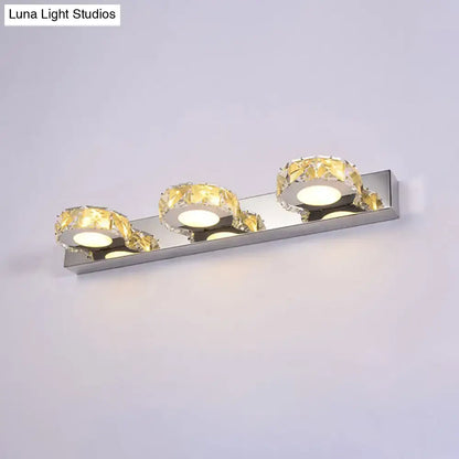 Modern chrome and gold crystal vanity sconce with three crystal-encrusted light fixtures emitting warm glow
