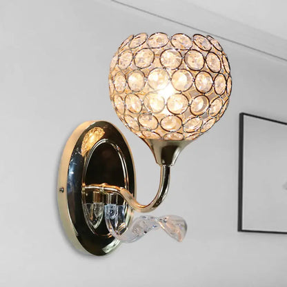 Modern wall sconce with gold-toned finish, spherical crystal globe, and clear glass accent for bedroom lighting