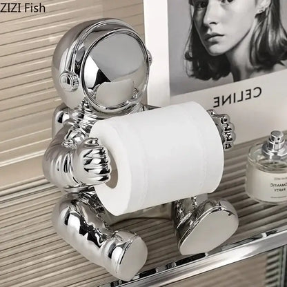 Shiny chrome astronaut tissue box figurine holding a roll of toilet paper for modern living room decor