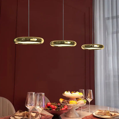 Three sleek gold-finished decorbites circular dining pendant led lights hang above a modern dining table
