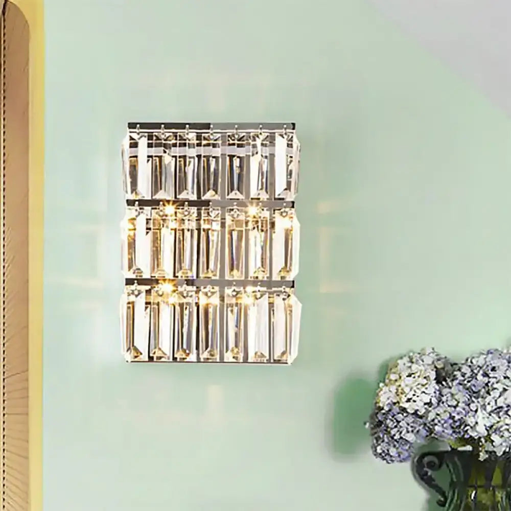 Modern chrome clear crystal wall lamp with three rows of faceted prisms in a sleek rectangular bedroom sconce