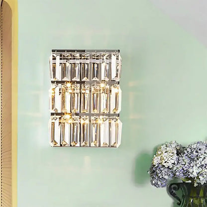 Modern chrome clear crystal wall lamp with three rows of faceted prisms in a sleek rectangular bedroom sconce