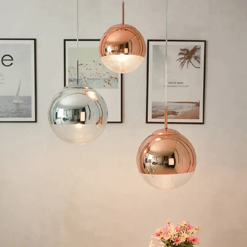Three modern chrome and copper glass ball led pendant lights with mirrored rose gold and clear glass finishes hang in a dining room
