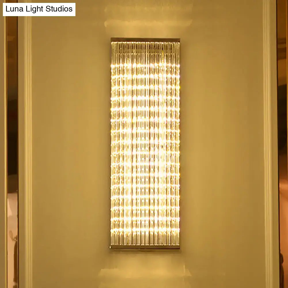 Modern chrome crystal led wall sconce with vertically aligned crystals emitting warm golden glow for living room bar light