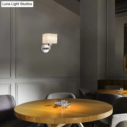 A modern chrome wall sconce light with a cylindrical glass shade and polished finish for hallway wall mount