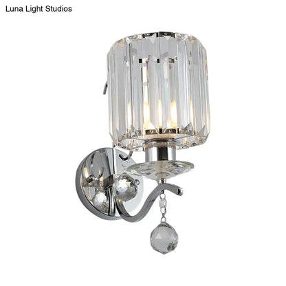 A modern chrome cylinder wall light fixture with clear crystal shade and dangling cut-glass pendant for bedroom lighting