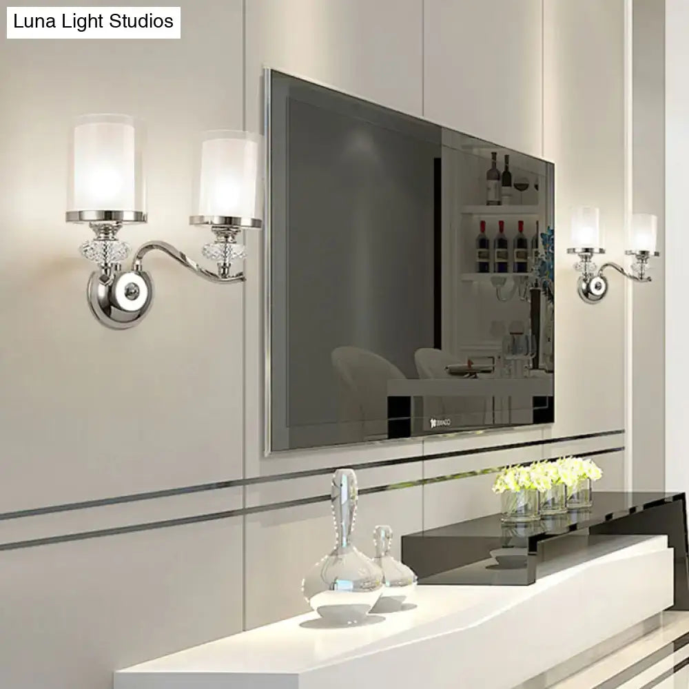 Modern chrome dual cylinder bathroom sconce with silver-toned fixture height, frosted glass shades, curvy arm, and crystal accents