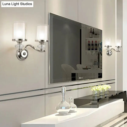Modern chrome dual cylinder bathroom sconce with silver-toned fixture height, frosted glass shades, curvy arm, and crystal accents