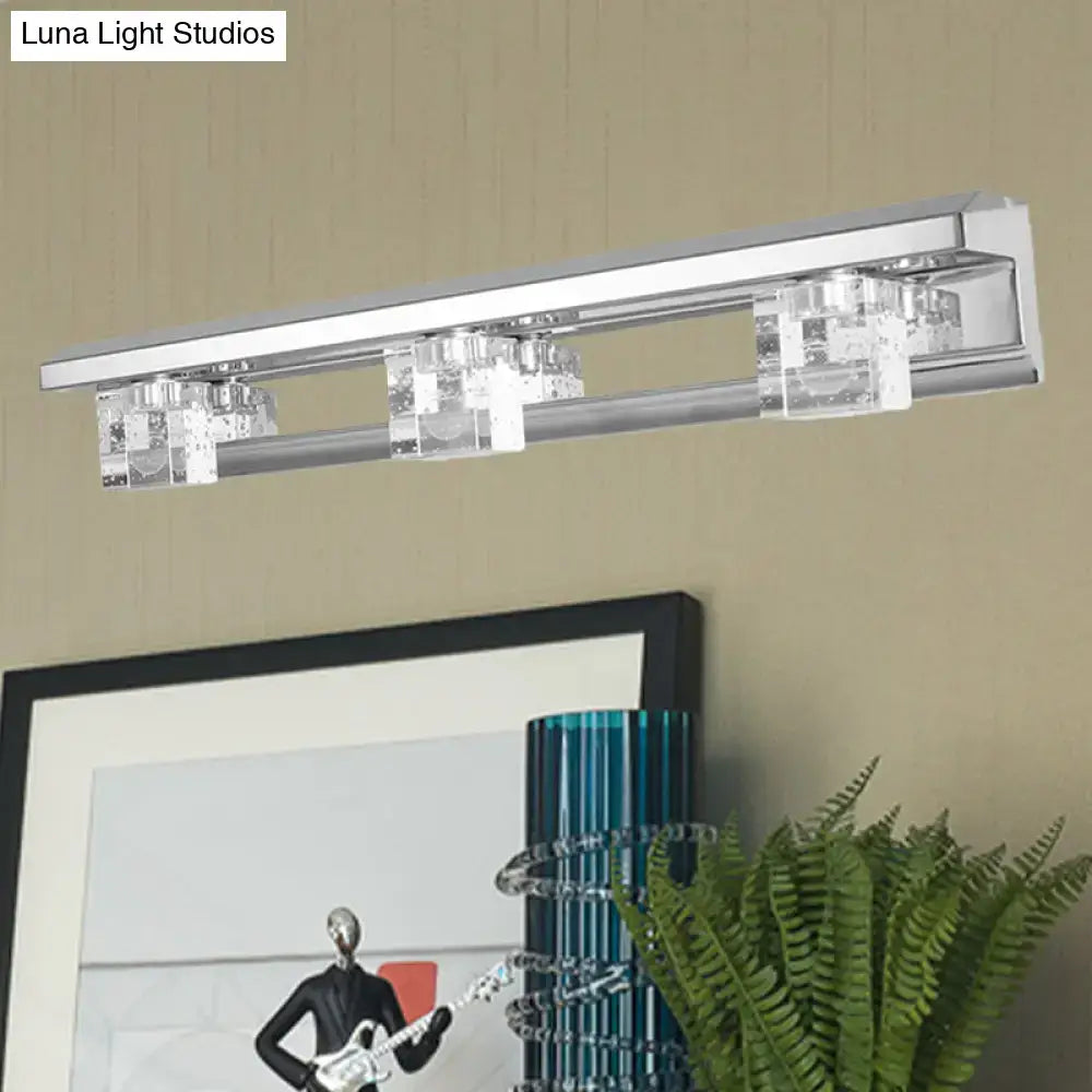 Modern chrome finish wall-mounted vanity sconce with three clear crystal cubes emitting warm white light for bathroom use