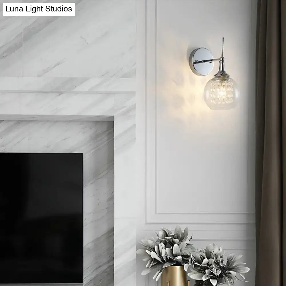 A modern chrome finish wall lamp with a polished chrome finish and crystal inner glass for bedroom lighting
