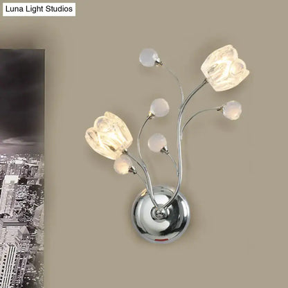 Modern chrome wall lamp with swirling arm, three illuminated glass flower shades, and four frosted crystal orbs