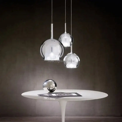 Modern chrome glass bubble pendant lights with spherical design hang above a white table for dining room decorbites