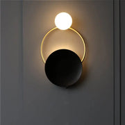 Modern circle wall sconce with a glowing white sphere suspended above a gold ring and matte black disc for bedroom lighting
