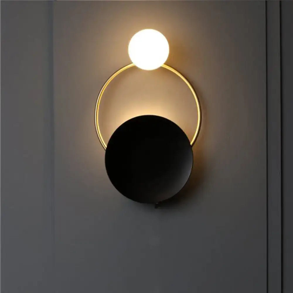 Modern circle wall sconce with a glowing white sphere suspended above a gold ring and matte black disc for bedroom lighting