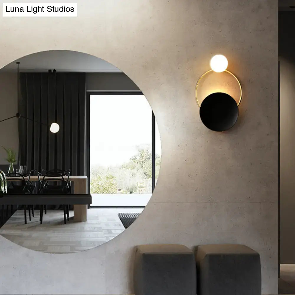 Modern circle wall sconce with sleek gold-toned frame black matte disc and illuminated white globe bulb for bedroom lighting