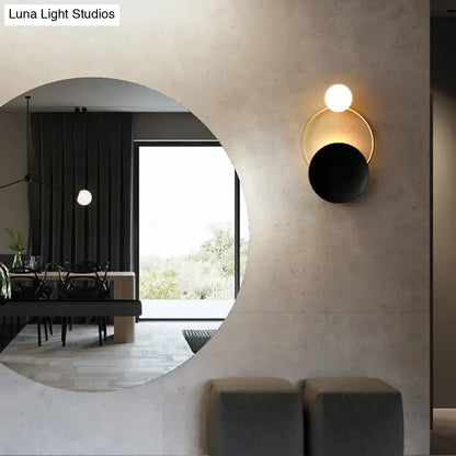 Modern circle wall sconce with sleek gold-toned frame black matte disc and illuminated white globe bulb for bedroom lighting