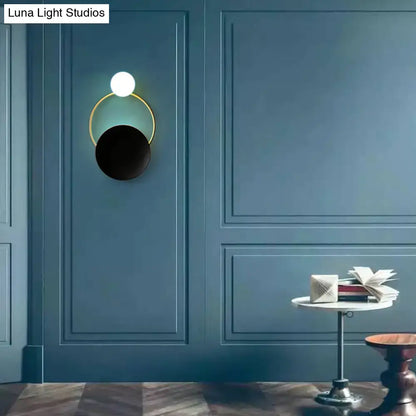 Modern circle wall sconce with a glowing white spherical bulb, matte black disc, and gold-toned ring for bedroom lighting