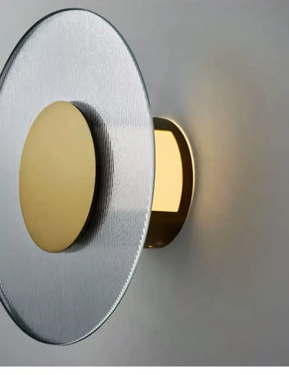 Modern circular brushed metallic wall lamp with a silver face and gold-toned light source for elegant glass wall decorbites decor