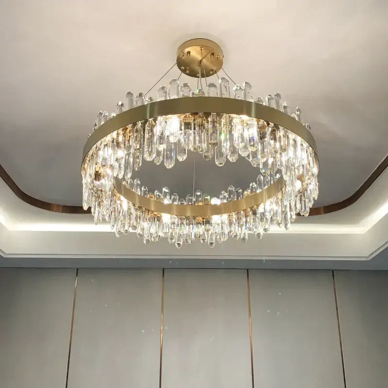 A modern circular gold decorbites crystal chandelier featuring double rings and cascading clear crystal prisms