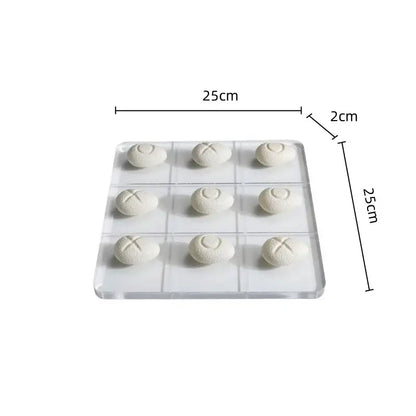 Modern clear acrylic tic tac toe board with white resin pebble chess pieces featuring engraved o and x marks for living room decor