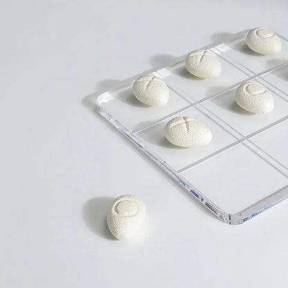 Modern clear acrylic tic tac toe board with white textured resin pebble chess pieces for living room decor