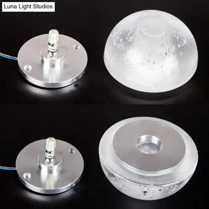 Modern wall light with clear bubble crystal textured dome and silver base emitting warm white light for living room use