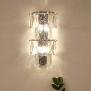 A modern clear crystal tiered wall lamp with polished chrome frame included in lamp kit for bedroom use