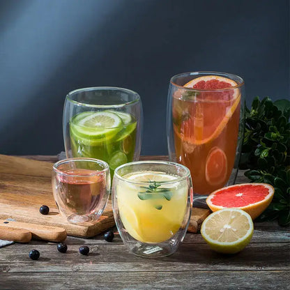 Set of modern clear double wall borosilicate glass tumblers with citrus slices and herbs in colorful beverages
