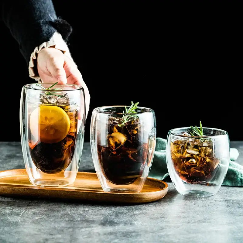 Set of three clear modern double wall glass cups with ice lemon slices and rosemary for dining room use