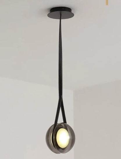 Black leather strap suspends a sleek smoked glass decorbites designer pendant light with illuminated bulb for bedroom decor