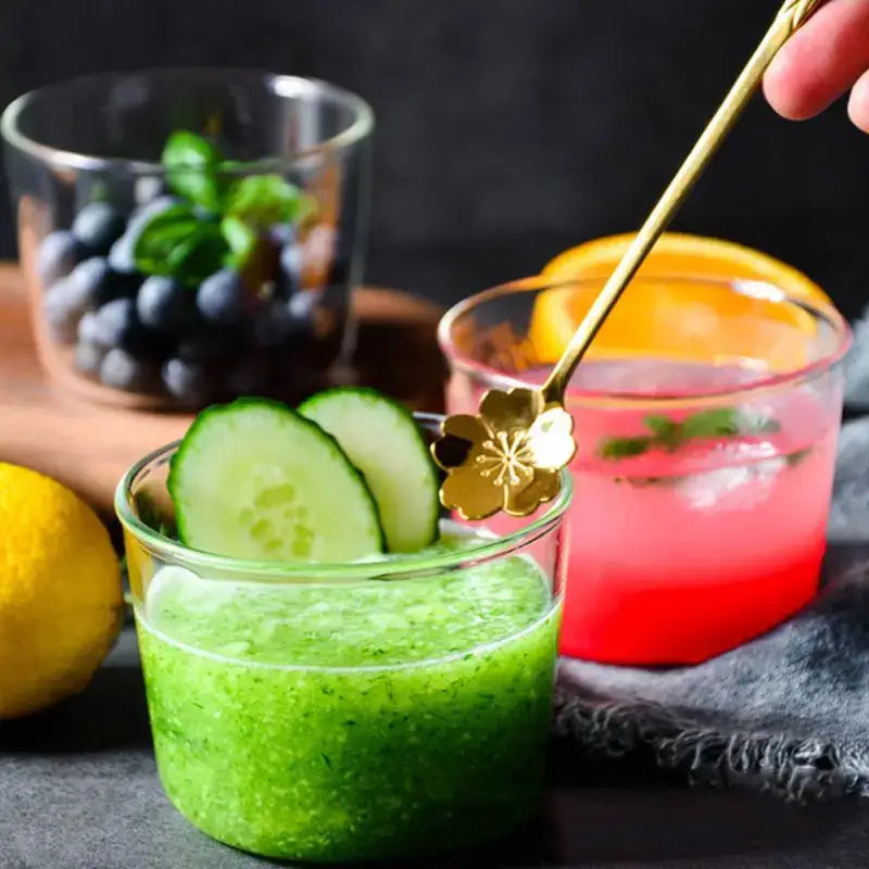 Gold flower-shaped spoon with slender handle resting in vibrant green cucumber juice in modern clear glass dessert cup set