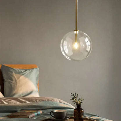 Modern pendant light featuring a clear transparent glass globe with a brass-finished gold kitchen rod suspension