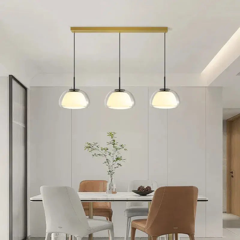 Modern clear glass jelly pendant lamp with three spherical shades suspended from a gold-toned bar for living room