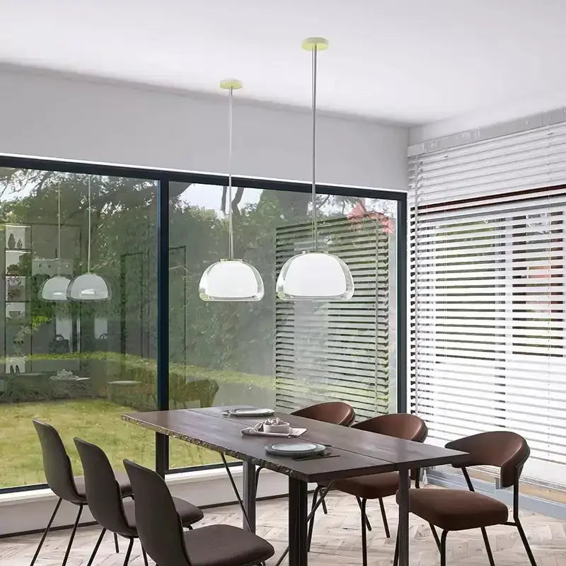 Two modern clear glass jelly pendant lamps with dome-shaped shades and metallic chains hang above a dining table